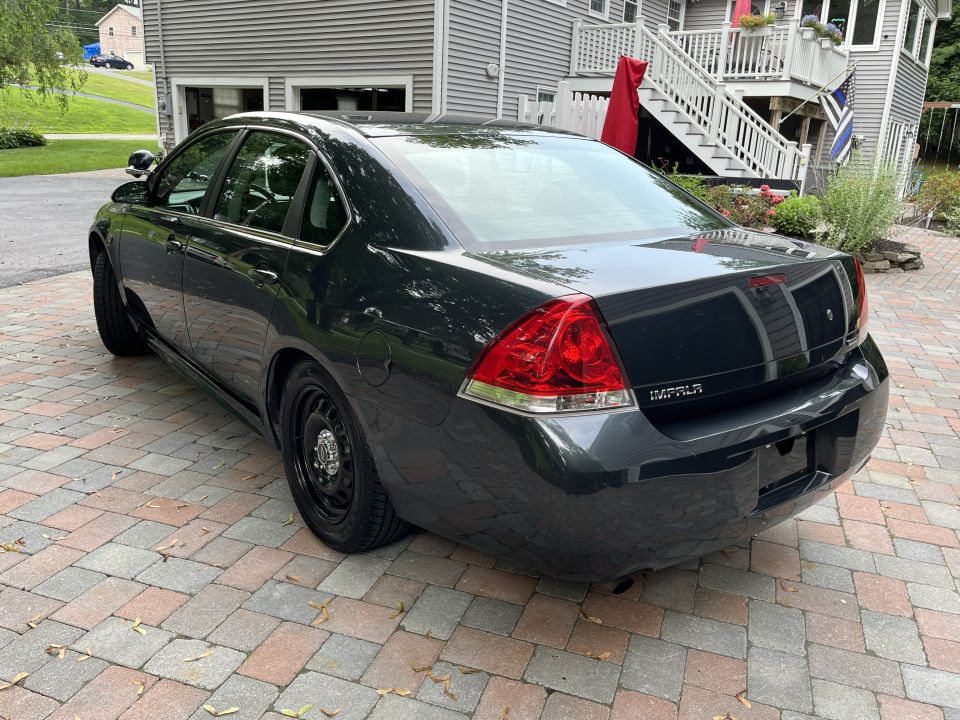 Dark gray sedan parked on a brick driveway, rear passenger side view.