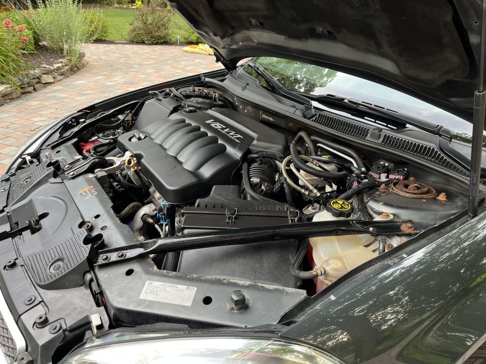 Dark colored car engine bay with V6 VVT engine cover visible.