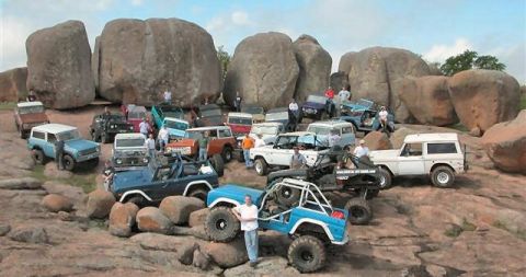 1973 Ford Bronco - Many off-road vehicles and people are gathered on a rocky terrain with large boulders in the background.