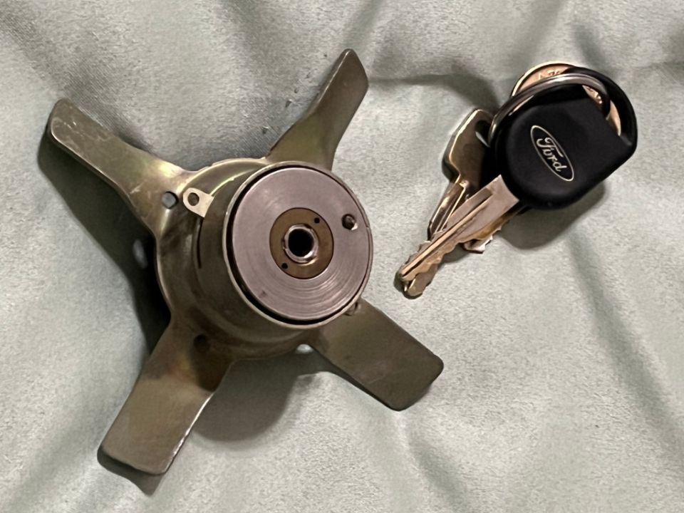 Metal propeller part and Ford car keys on a textured surface.