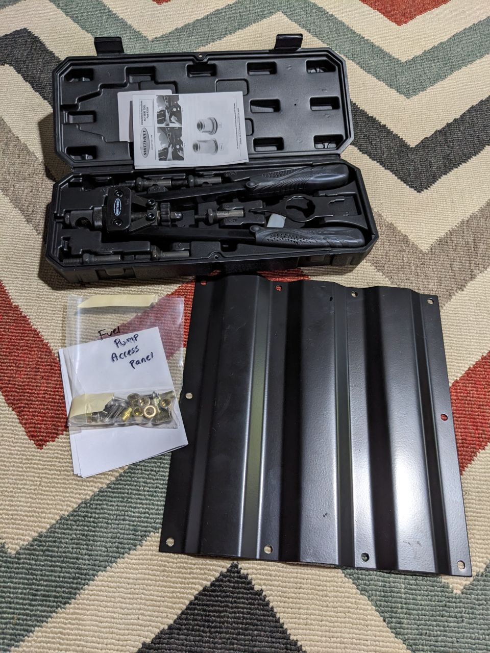 Fuel pump access panel tool kit and panel on a rug.