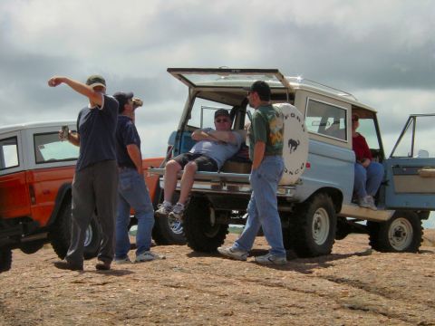 1973 Ford Bronco - Group of people gathered around a light blue Ford Bronco, with an orange Bronco in the background.