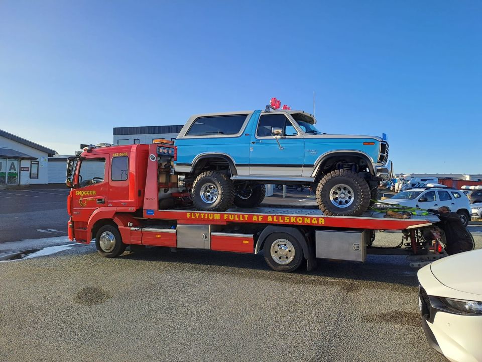 Blue and white lifted Ford Bronco loaded on a red Icelandic flatbed tow truck