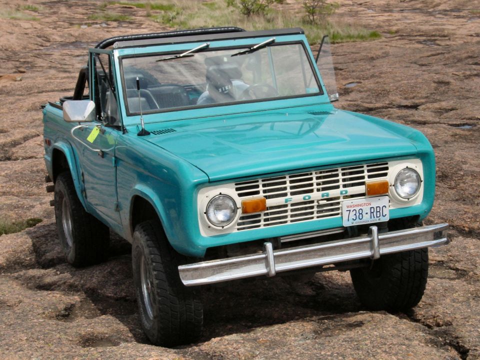 Teal early Ford Bronco convertible on bare rock, top removed, Washington plate