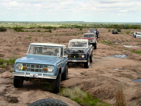 1973 Ford Bronco - Several Ford Broncos navigate a rocky landscape under a cloudy sky.
