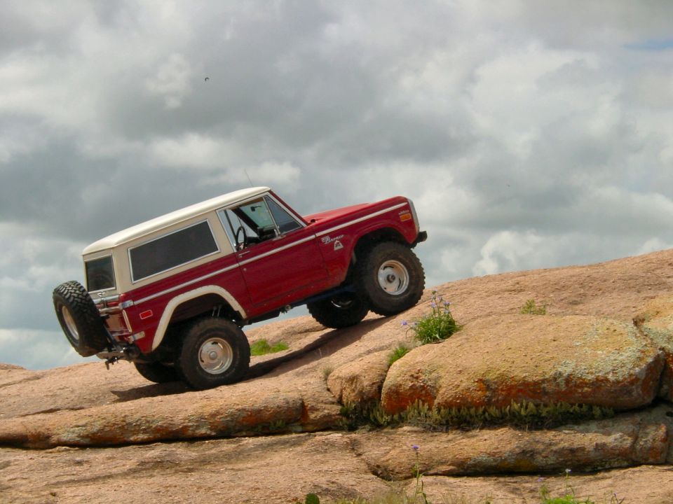 Red and white Ford Bronco climbing a rocky hill, with a spare tire mounted on the rear