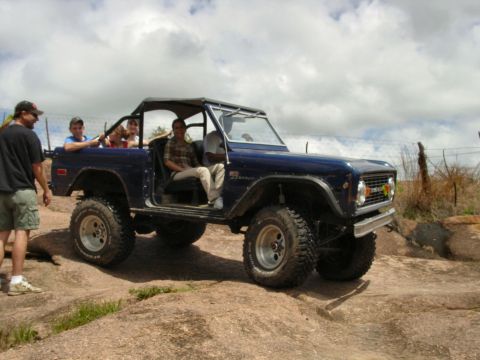 1973 Ford Bronco - A blue 1973 Ford Bronco navigates a rocky terrain with several people inside.