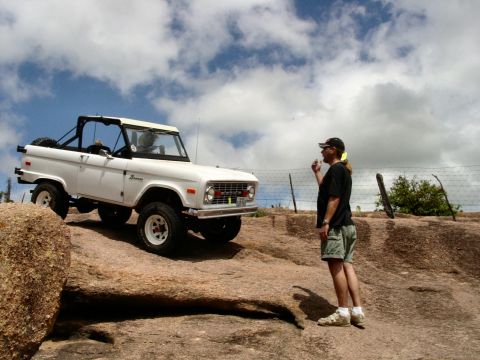 1973 Ford Bronco - White 1973 Ford Bronco navigating rocky terrain under a cloudy sky.
