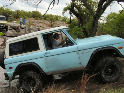 1973 Ford Bronco - A light blue 1973 Ford Bronco navigates a rocky, muddy trail with a driver behind the wheel.