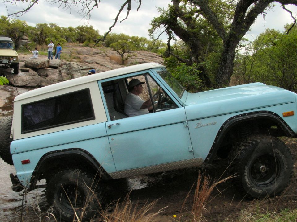 Light blue 1973 Ford Bronco driving through mud and rocks with a person inside