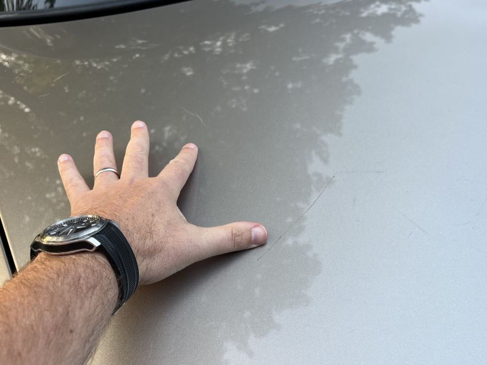 Hand on a Ford Crown Victoria hood showing a paint scratch