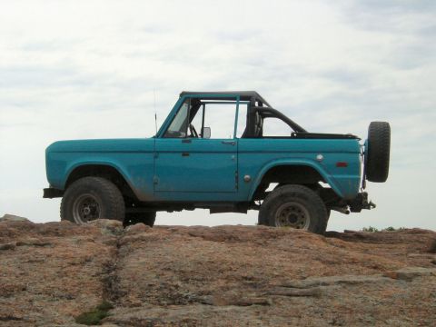 1973 Ford Bronco - A classic blue 1973 Ford Bronco is parked on a rocky outcrop under a cloudy sky.