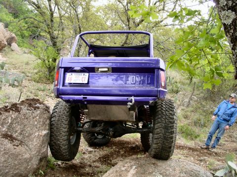 1973 Ford Bronco - A man watches as a lifted purple Ford Bronco navigates a rocky off-road path.