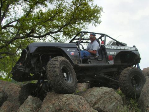 1973 Ford Bronco - A modified black Ford Bronco navigates a rocky terrain, demonstrating its off-road capabilities.