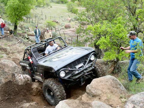 1973 Ford Bronco - An off-road vehicle tackles a challenging rocky course with spectators watching.