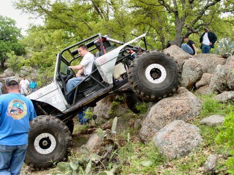 1973 Ford Bronco - A heavily modified off-road vehicle attempts to climb a steep, rocky terrain with spectators watching.