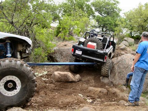 1973 Ford Bronco - A black 1973 Ford Bronco with a roll cage navigates rocky terrain, assisted by another off-road vehicle.