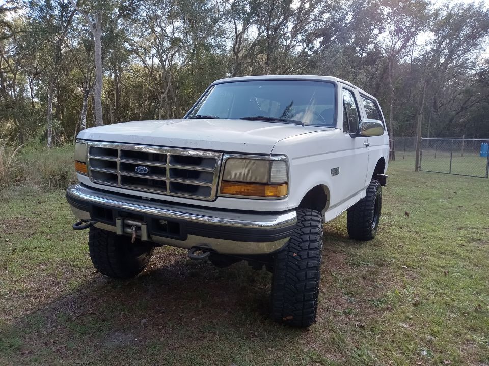 White 1994 Ford Bronco with off-road tires and front winch parked outdoors.