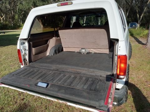 1994 Ford Bronco - The open tailgate of a pickup truck reveals the bed, covered by a white camper shell.