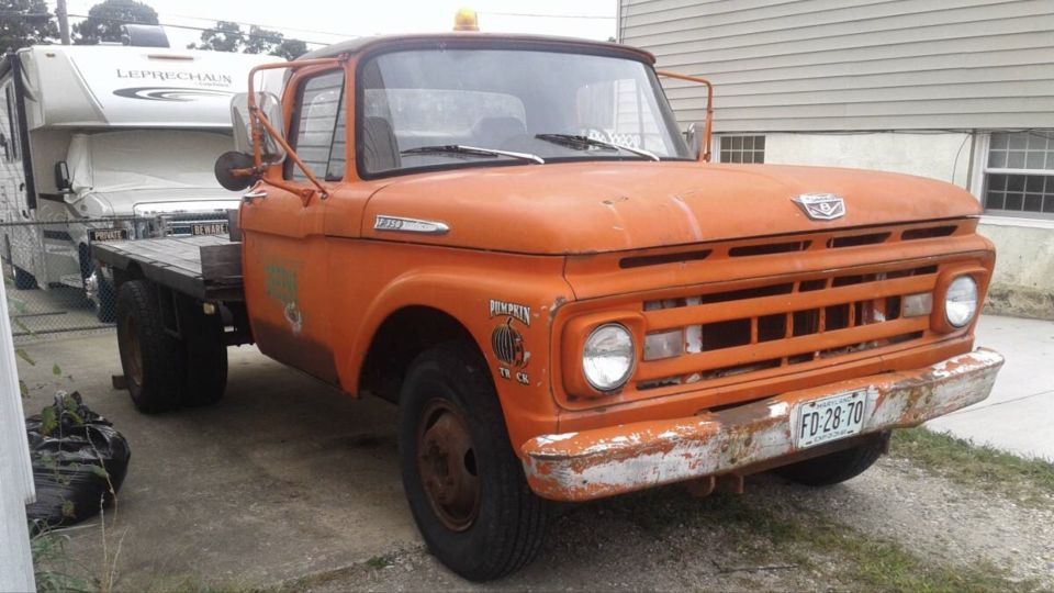 Orange 1961 Ford F-350 flatbed truck towing an RV