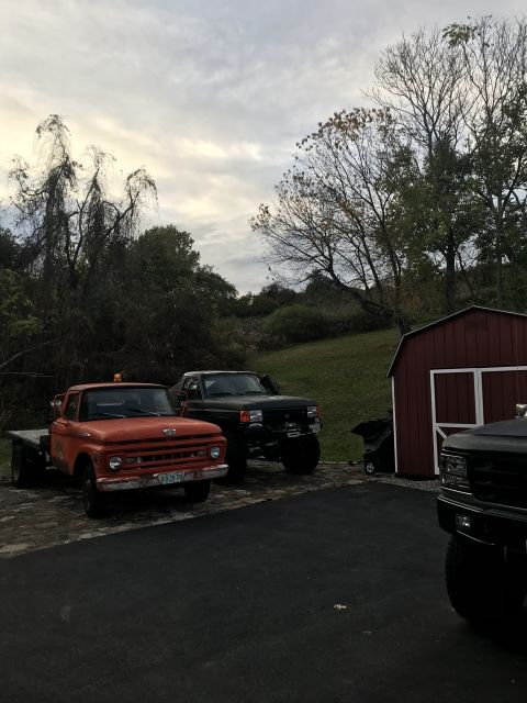 1961 Ford F-350 - Three pickup trucks are parked in a driveway next to a red barn under a cloudy sky.