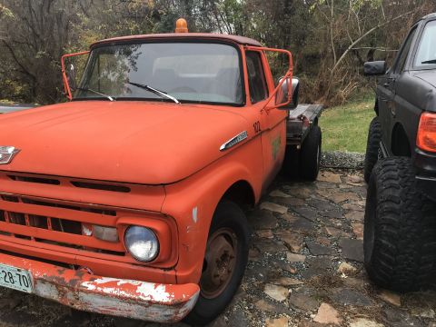 1961 Ford F-350 - An orange tow truck with a flatbed is parked next to a dark-colored truck.
