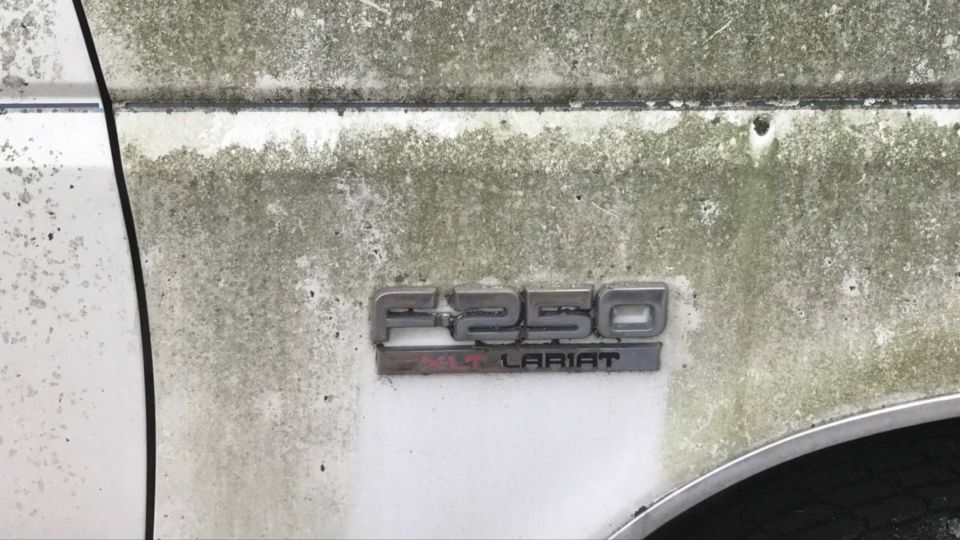 F-250 Lariat badge on a weathered white truck door