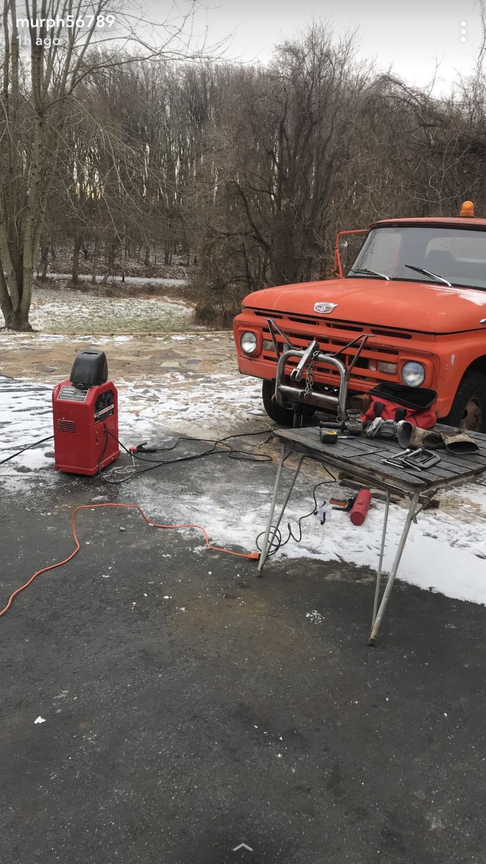 Orange truck with a plow mount, welding machine, and table with tools nearby