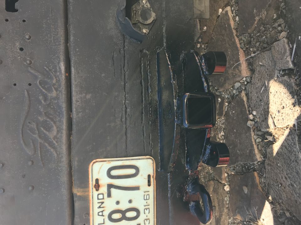 License plate dated 3-31-61 and a black hitch receiver on a rusty vehicle frame