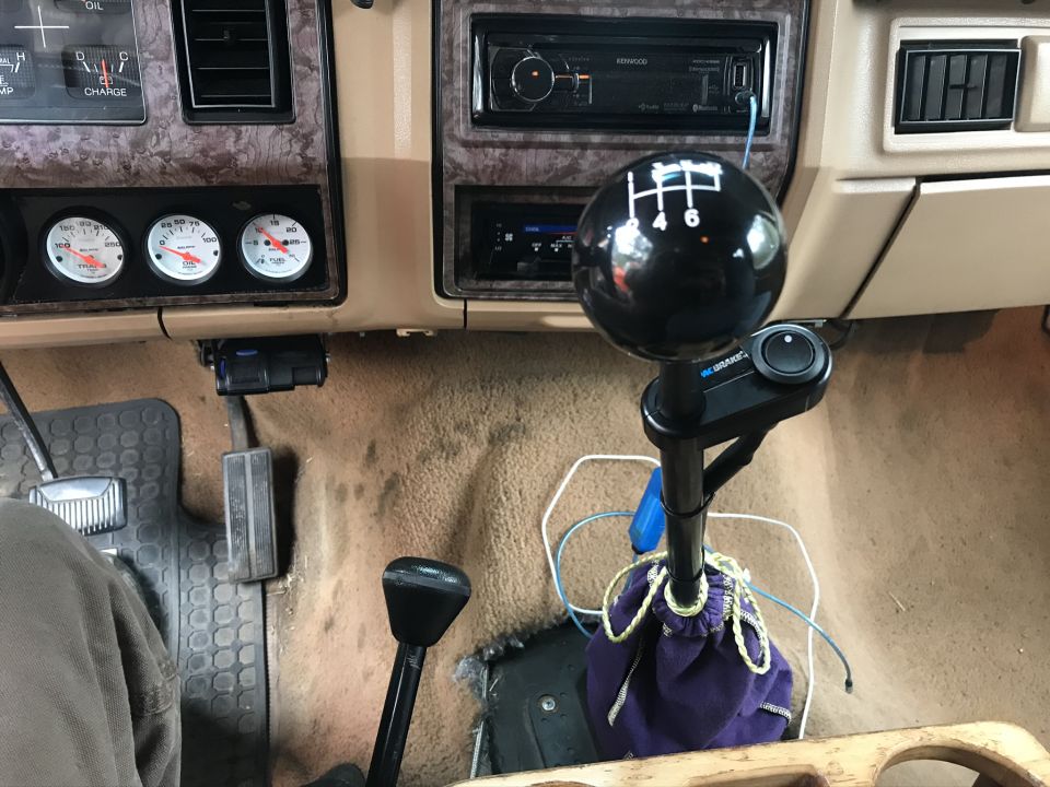 Black 5-speed manual shift ball with aftermarket gauges on a tan dashboard interior