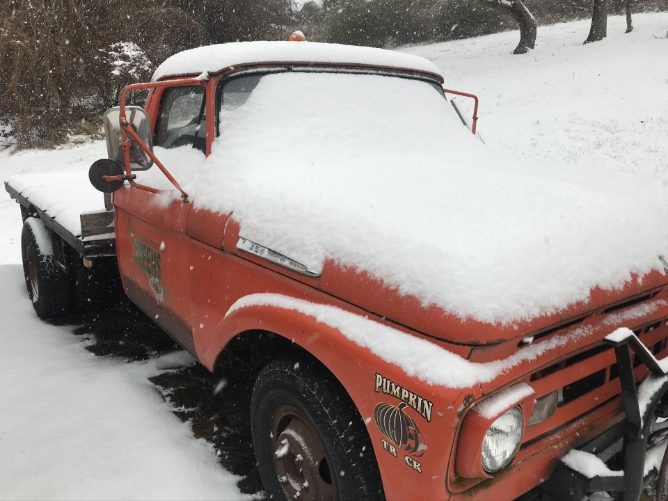 1961 Ford F-350 flatbed truck covered in snow, with 'Pumpkin Truck' decal on the door