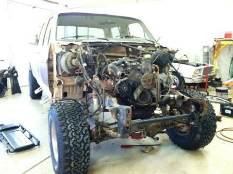1985 Ford F-350 - Truck chassis with engine removed, revealing the engine bay and front suspension components. A second vehicle is partially visible in the b…