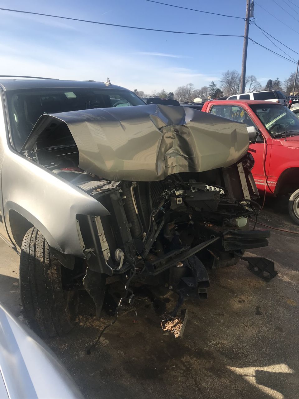 Silver SUV with heavily crumpled front end, radiator exposed, parked outdoors