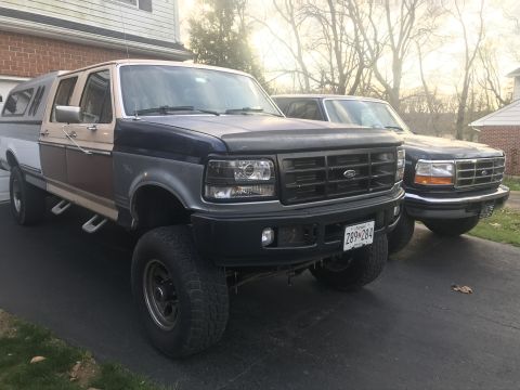 1995 Ford F-150 - Two Ford trucks, including a 1995 F-150, are parked in a driveway. The F-150 has a two-tone paint scheme and aftermarket wheels.