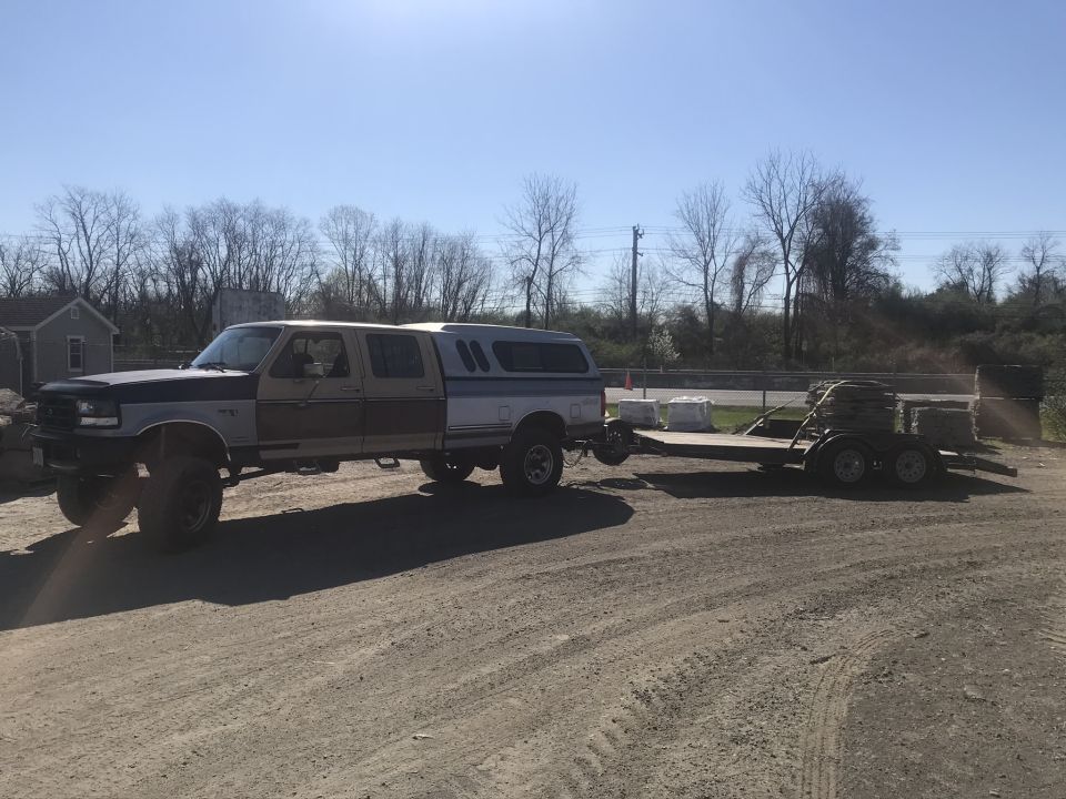 Ford pickup truck with a camper shell towing a flatbed trailer loaded with materials