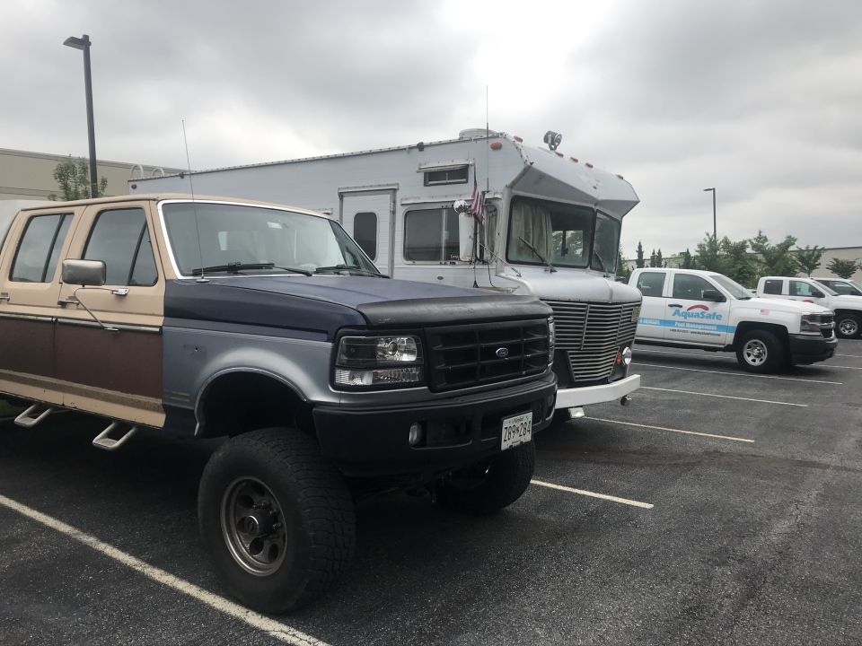Ford pickup truck with two-tone paint and RV parked behind it. Other trucks are visible in the background