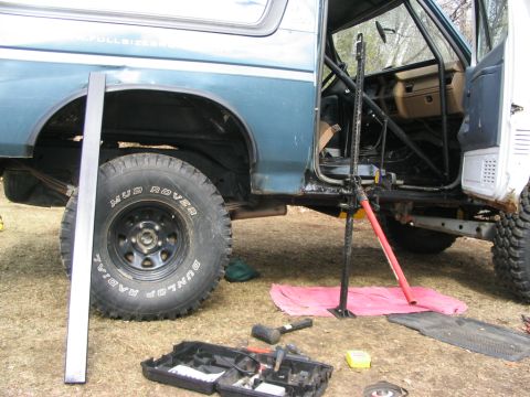 1986 Ford Bronco - A 1986 Ford Bronco is shown with its doors open and a jack supporting the frame, surrounded by tools and parts.