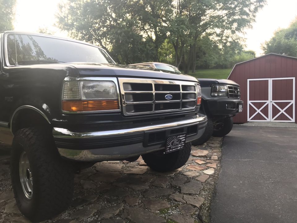 Front view of a dark Ford F-Series pickup truck with a chrome grille and bumper, parked in front of a red barn.