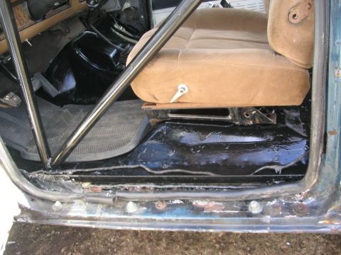 1986 Ford Bronco - The interior floor of a vehicle shows wear and tear, with a roll cage installed for added support.