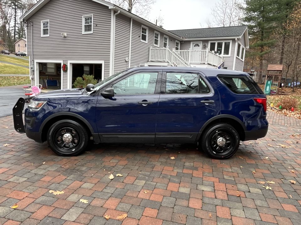 Dark blue Ford Police Interceptor Utility SUV parked on a brick driveway, side view
