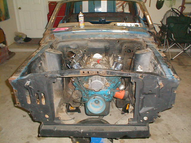 1967 Ford Mustang engine bay with blue engine, rust, and missing parts