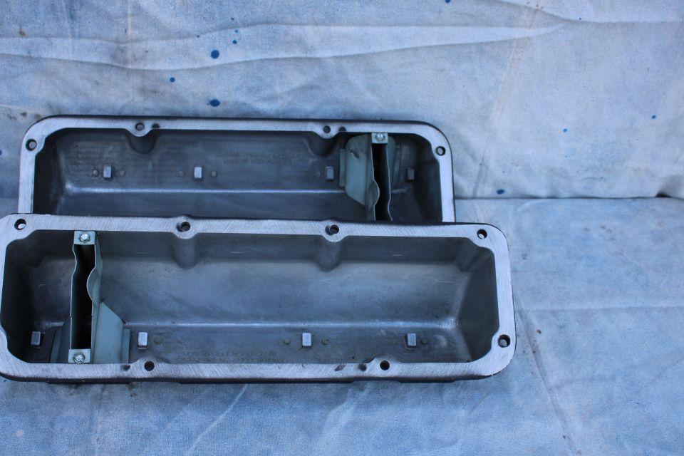 Two aluminum V8 engine valve covers on a blue-splattered surface.