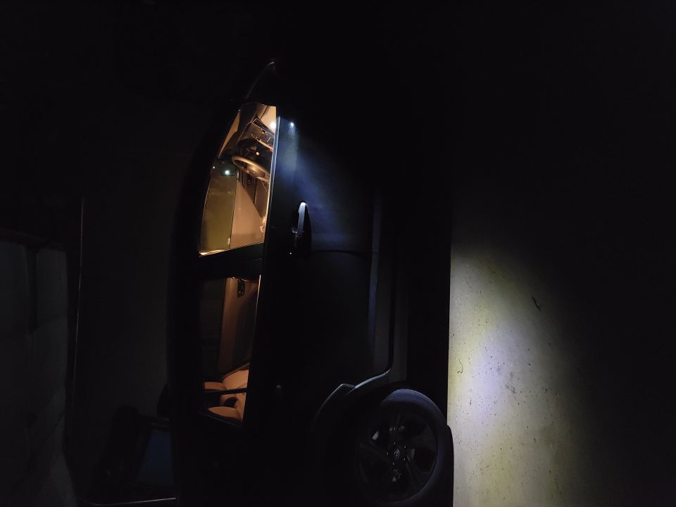 Interior of a vehicle with open door, illuminated by light. Wheel visible on the right.