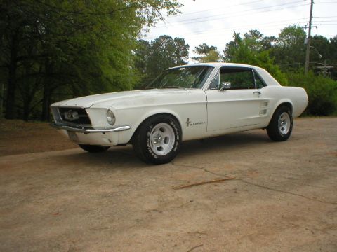 1967 Ford Mustang - A white 1967 Ford Mustang coupe is parked outdoors on a concrete surface with trees in the background.