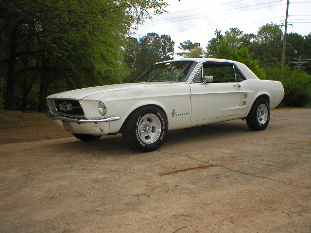 white 1967 Ford Mustang coupe parked on concrete, trees in background
