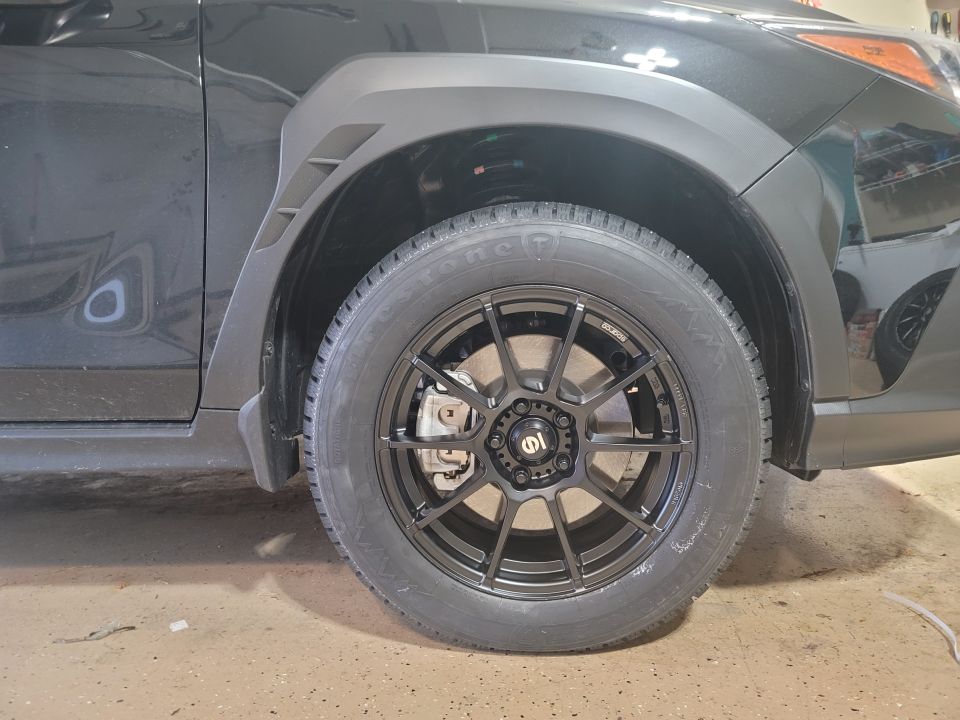 Black Subaru Impreza with aftermarket black wheels and fender flares, front passenger side view.