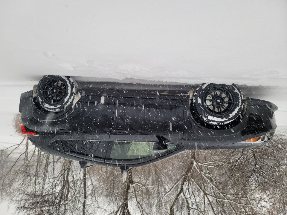 Overturned black Subaru Impreza hatchback in a snowy ditch during a snowstorm.