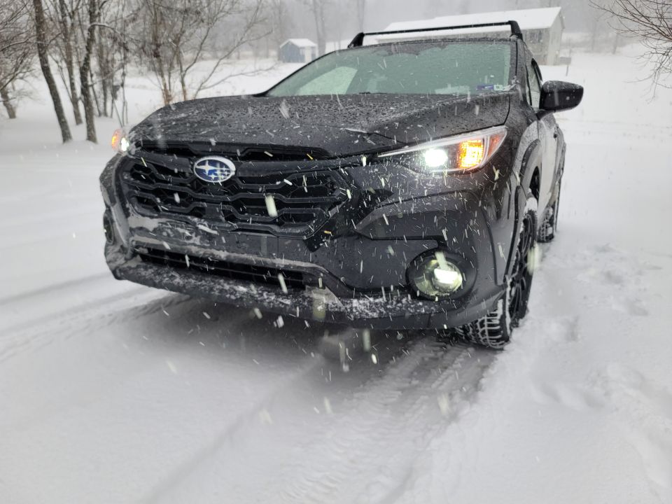 Dark gray Subaru SUV in falling snow, front view.