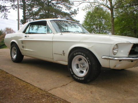 1967 Ford Mustang - A white 1967 Ford Mustang coupe is shown from a 3/4 front angle, highlighting its classic body style and chrome accents.
