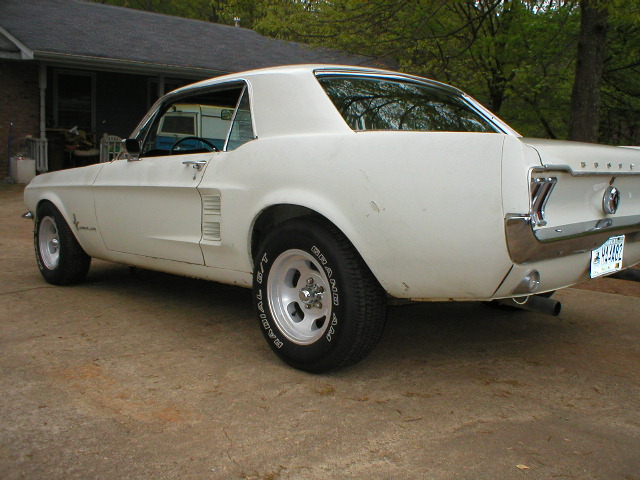 White 1967 Ford Mustang coupe parked on concrete, rear three-quarter view